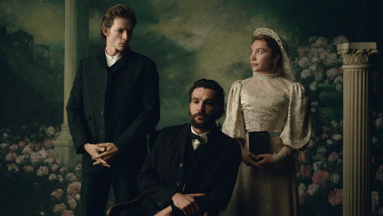 "Three people in Victorian-era clothing pose in a formal portrait setting with floral and classical column background; one man seated, one man standing, and a woman in a white dress holding a book."